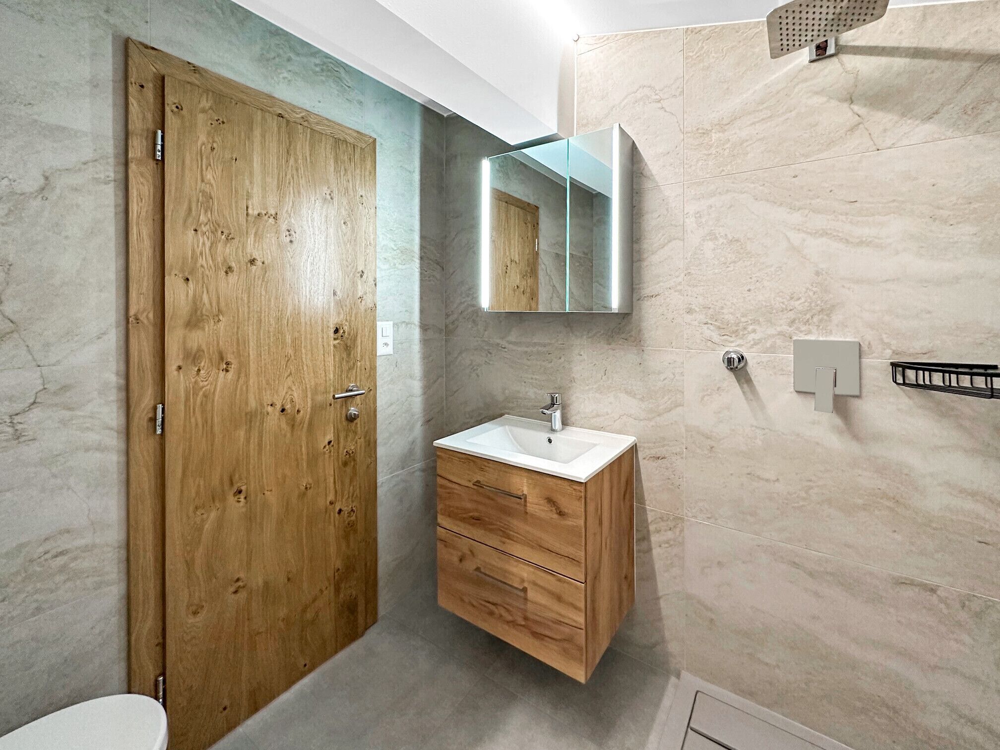 Une salle de bain avec une porte en bois, un meuble-lavabo en bois avec un évier, un miroir et des murs en marbre.