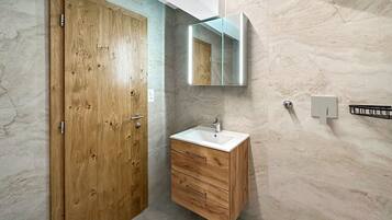Une salle de bain avec une porte en bois, un meuble-lavabo en bois avec un évier, un miroir et des murs en marbre.
