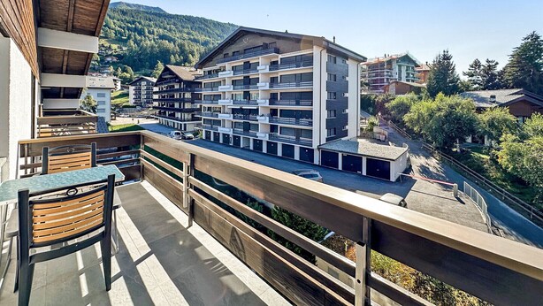 Un hotel moderno con varios balcones, un comedor con mesas al aire libre y vistas al paisaje montañoso circundante.