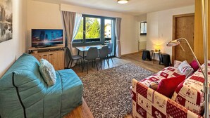 Una sala de estar con sofá, televisor, comedor con sillas y vistas al exterior.