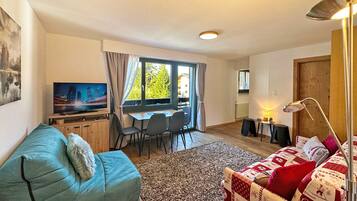 Una sala de estar con sofá, televisor, comedor con sillas y vistas al exterior.