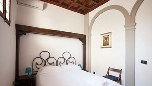 Un dormitorio con una cama con dosel, techo de madera, una mesita de noche con lámpara y una silla.