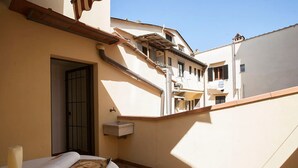 Un patio estrecho con suelo de baldosas, una pequeña zona de estar al aire libre con una mesa y un cuenco, y una puerta que da a un espacio interior.