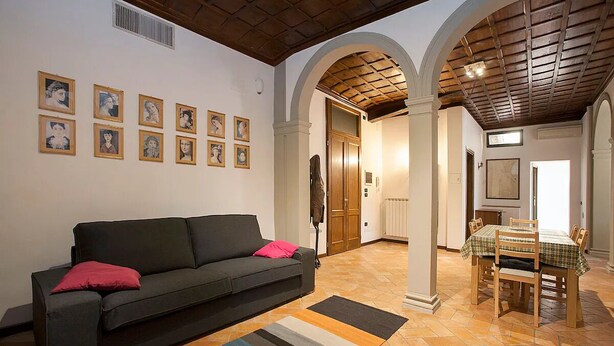 Una sala de estar con un sofá, una mesa de comedor con sillas y una alfombra estampada.