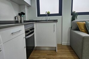A compact kitchen with white cabinets, a black countertop, and a window above the sink.