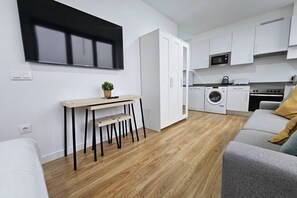 A modern kitchen with white cabinets, a microwave, a washing machine, and a dining area with a table and chairs.