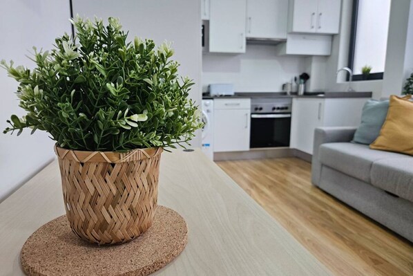 A modern kitchen with white cabinets, a dining area with a grey sofa, and a potted plant on a round cork coaster.