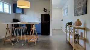 Moderni keittiö, jossa on keskeinen saareke, baarituolit, musta jääkaappi ja riippuvalaisin.