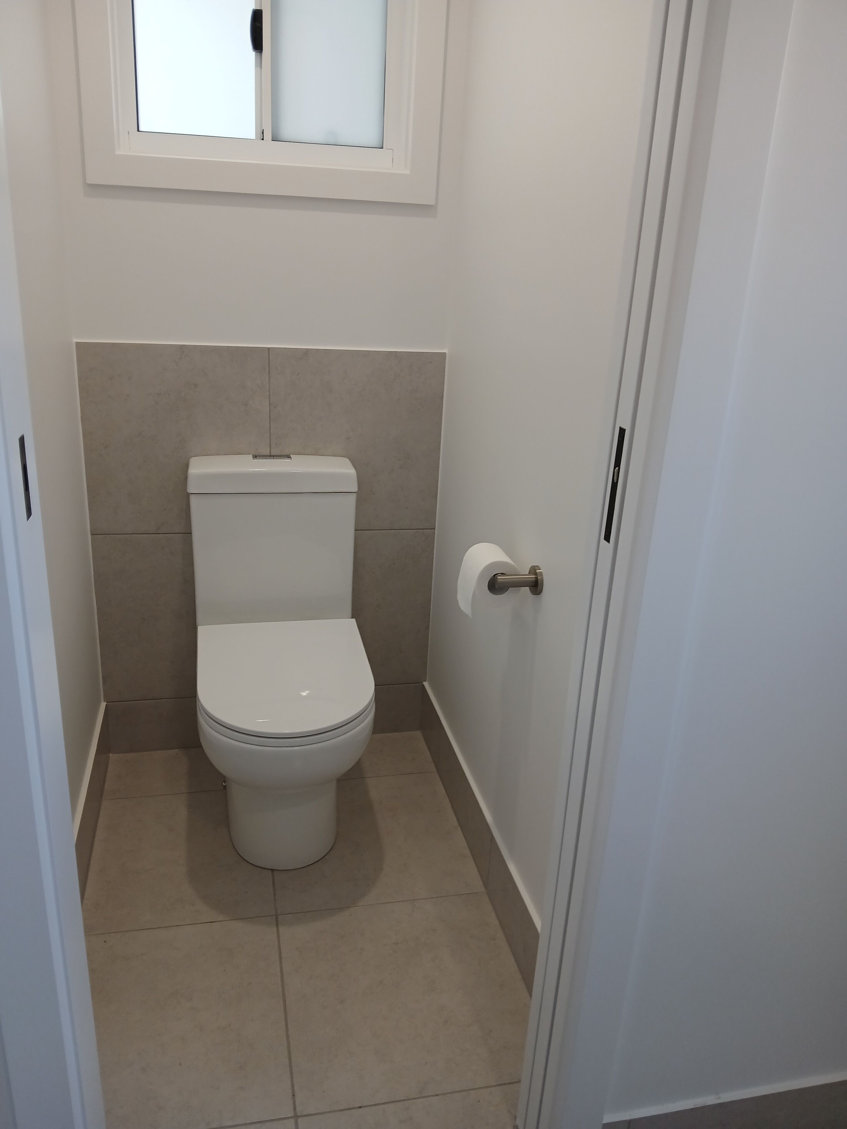 Un bagno piccolo e pulito con il water, un portasciugamani e una finestra sopra il water.
