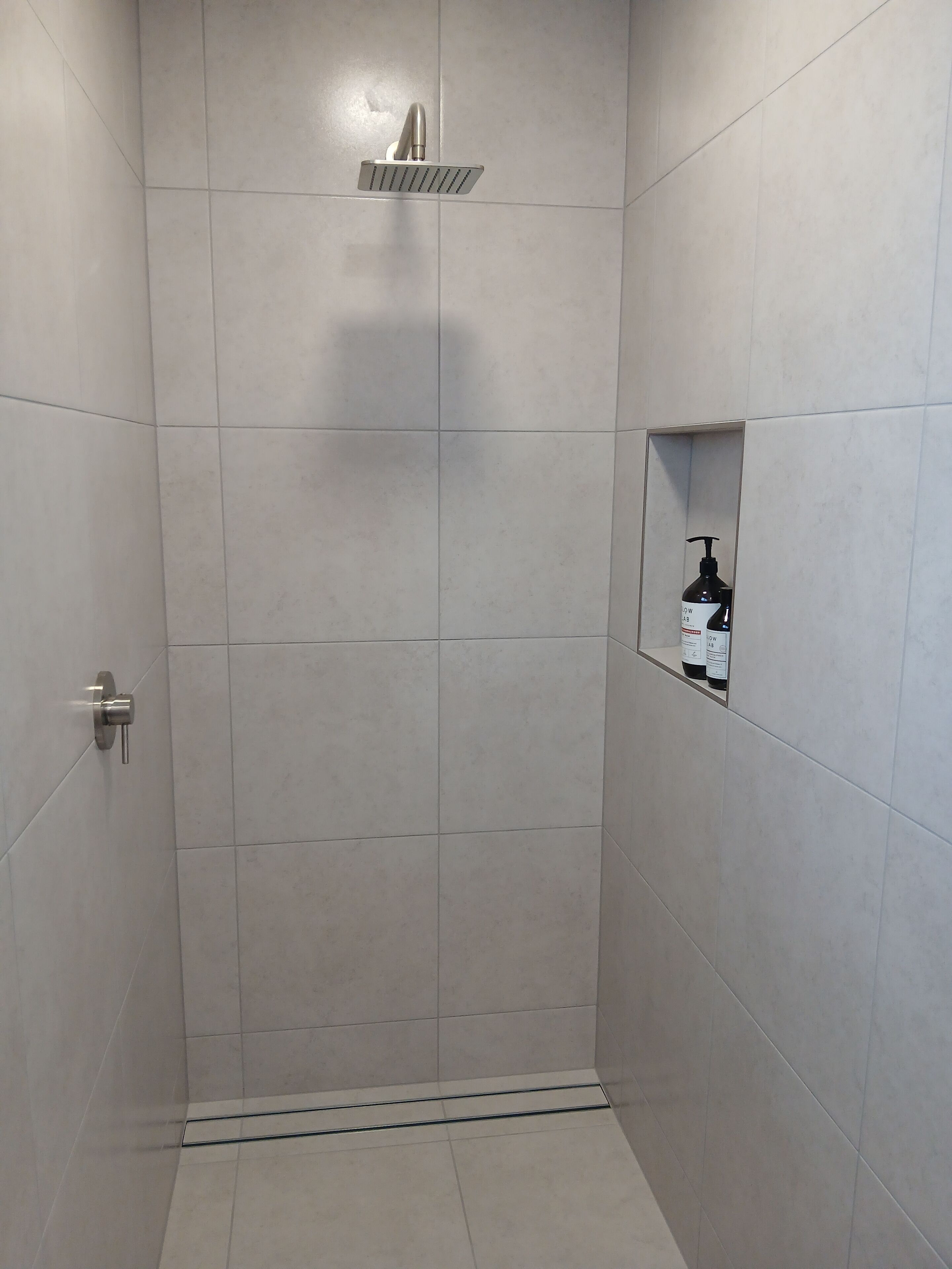 A shower area with a wall-mounted faucet, a small shelf with toiletries, and a door with a handle.