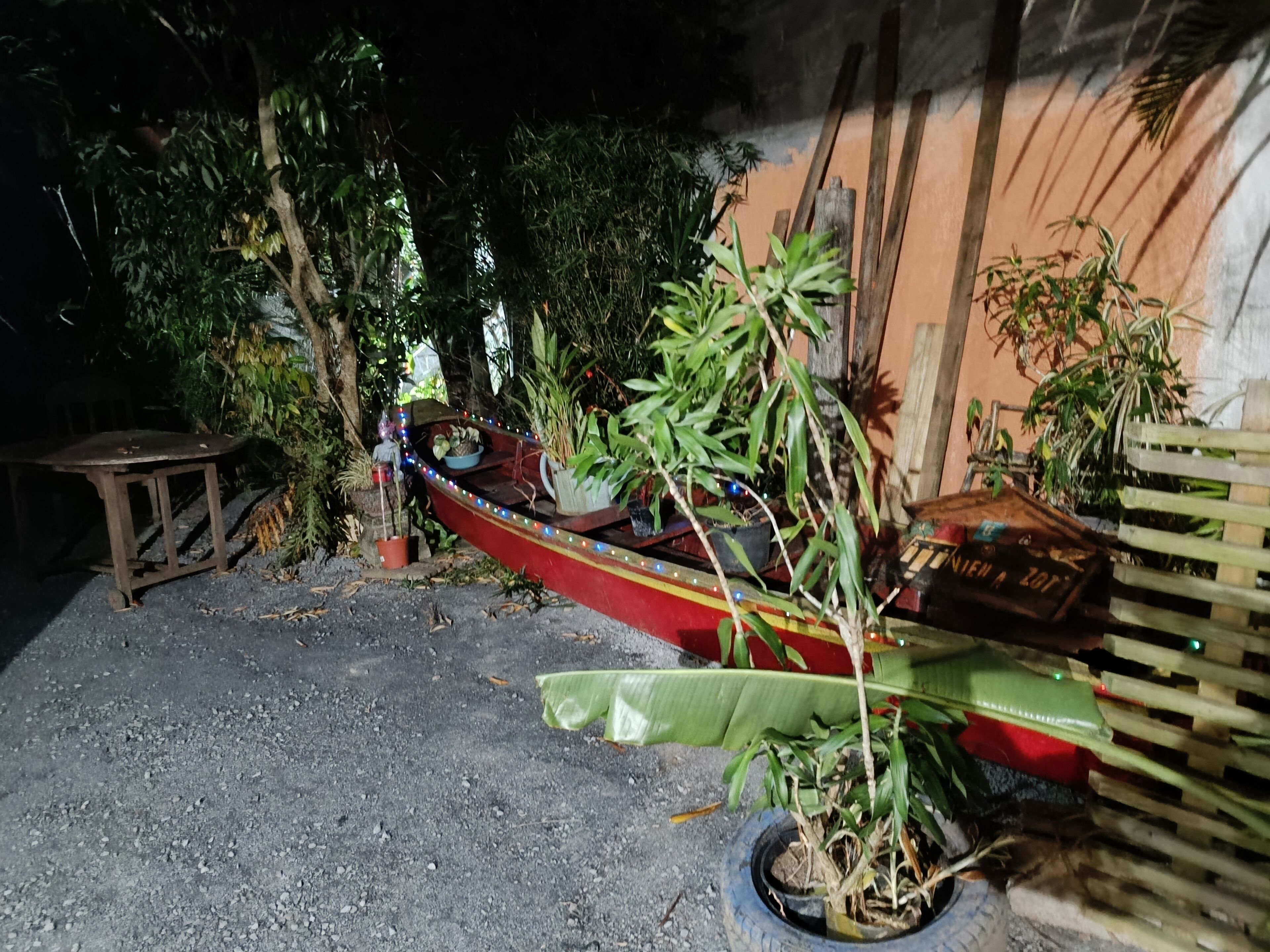 Un petit bateau à la coque rouge et à l’intérieur bleu, garé sur une surface recouverte de gravier.