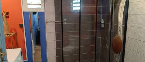 A bathroom with a glass shower enclosure, a washing machine, and a towel rack.