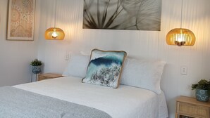 Une chambre à coucher avec un lit, un ventilateur de plafond, des œuvres d’art murales et deux lampes de chevet.