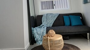 Un salon moderne avec un canapé gris foncé, deux coussins turquoise, un panier tressé avec un couvercle et un tapis à texture.