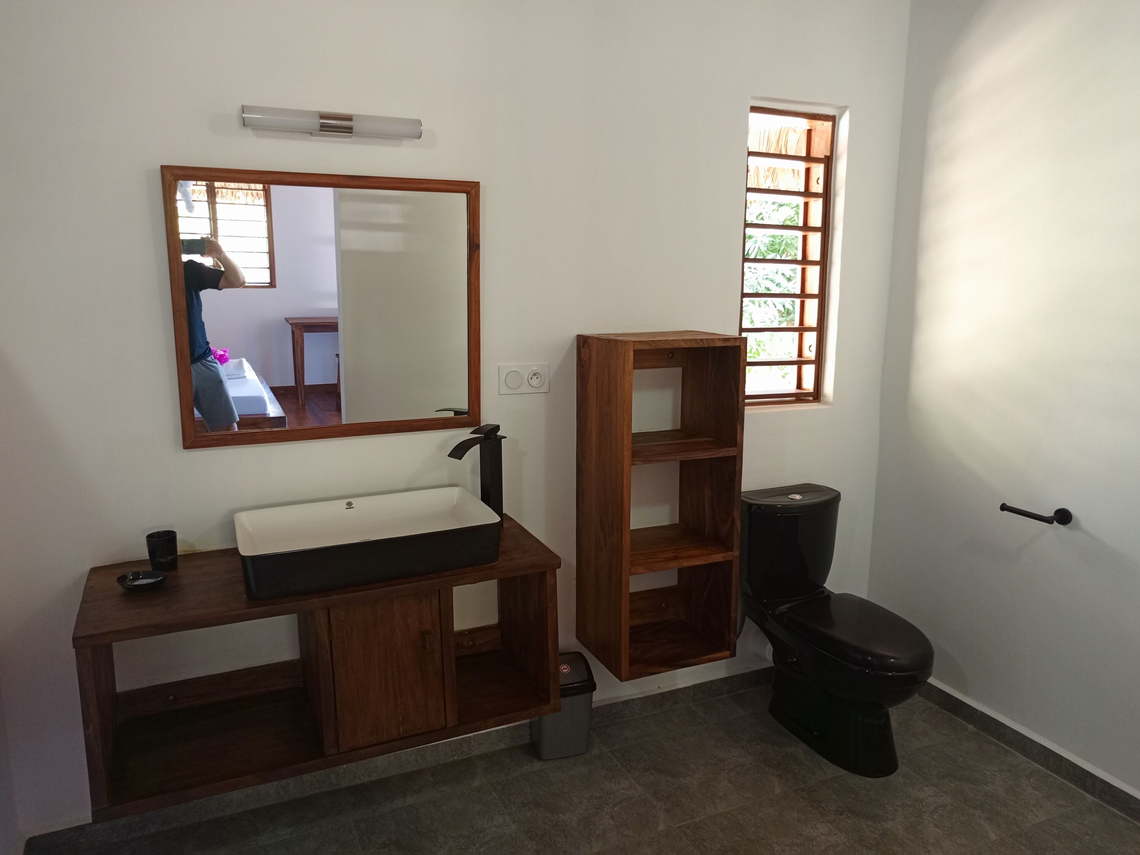 A bathroom with a wooden vanity, a mirror, a toilet, and a window.