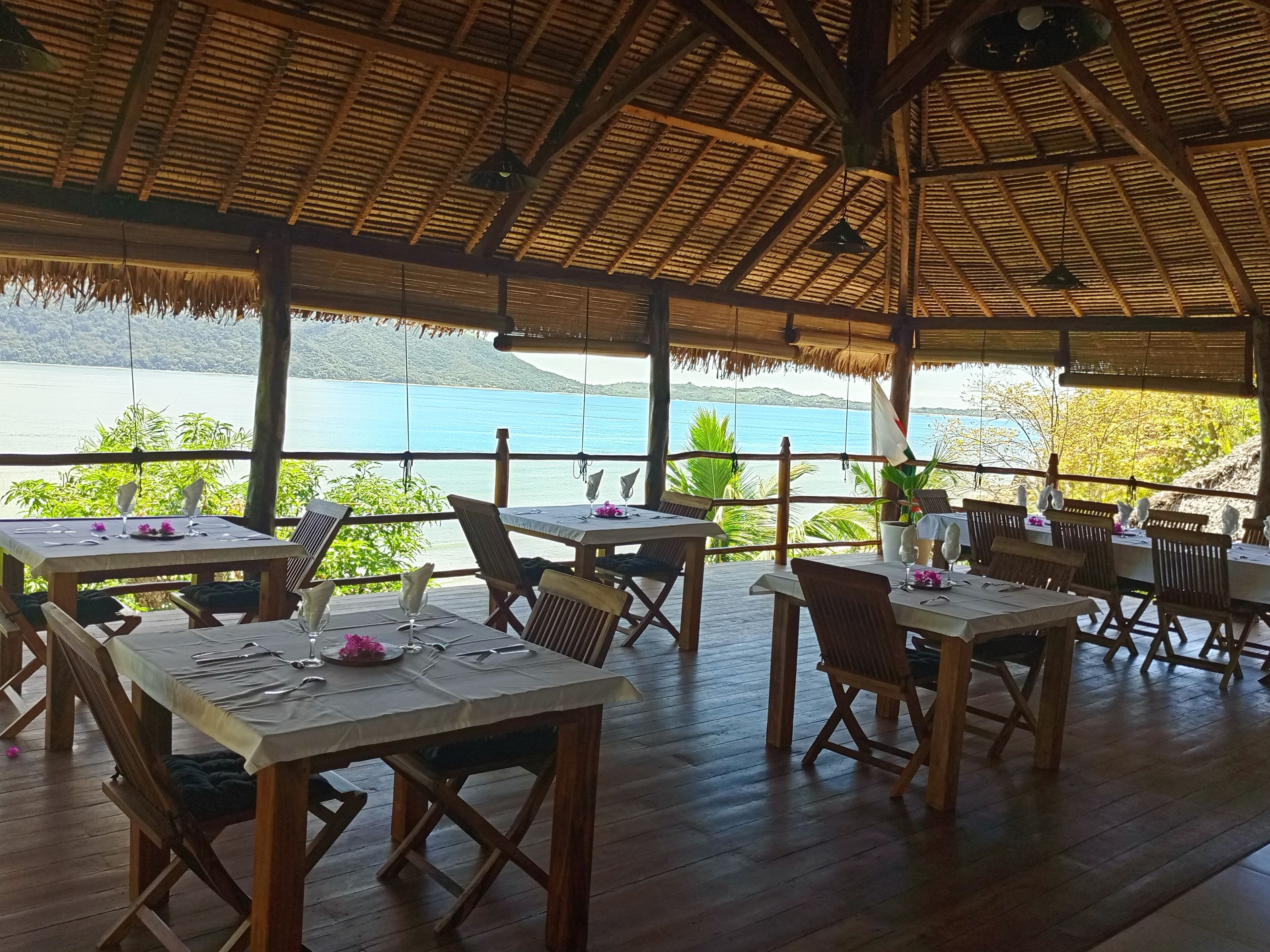 Un espace extérieur aménagé pour les repas, avec des tables et des chaises, offrant une vue sur un plan d’eau et la verdure.