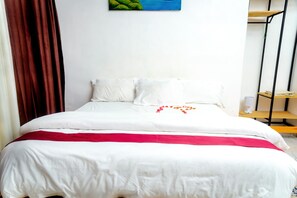 A neatly made bed with white bedding and a red blanket, a painting on the wall, and a shelf with items. - Esspasso  (Musanze)
