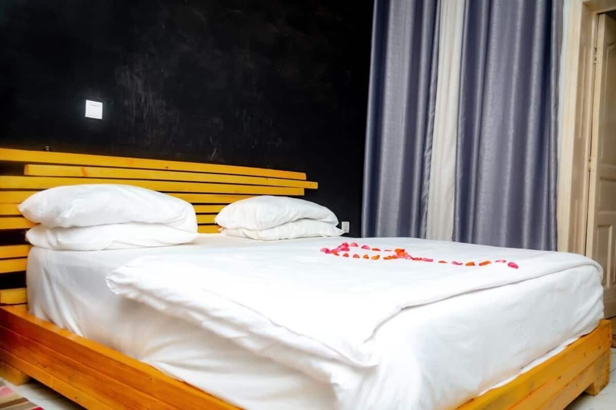 A bed with white bedding and pillows, a wooden headboard, and a window with curtains.