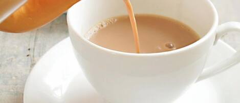 A white cup on a saucer with a hand pouring a light brown liquid into it.