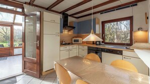Eine moderne Küche mit Holzbalken, einem Essbereich mit Tisch und Stühlen sowie einem Blick ins Freie durch große Fenster.
