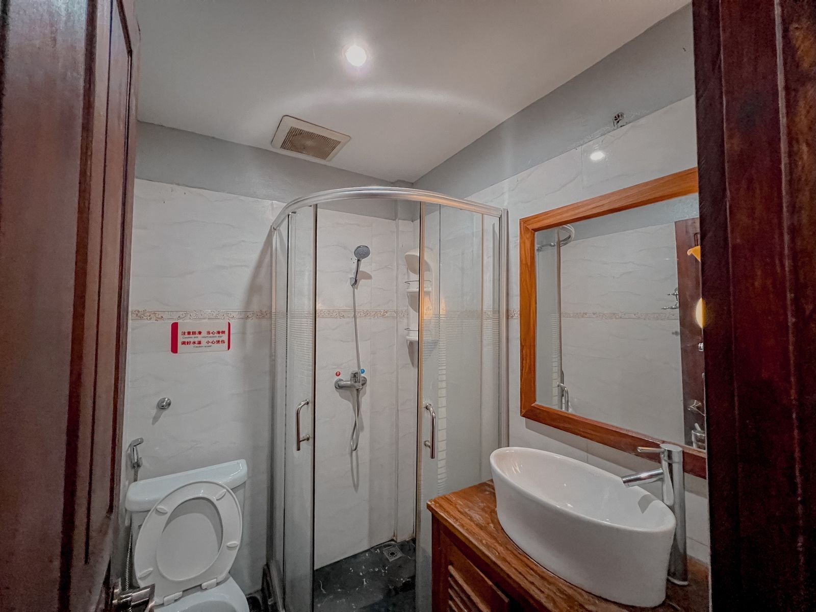 Une salle de bain avec une douche à parois de verre, des toilettes blanches et un meuble-lavabo en bois avec un lavabo blanc.