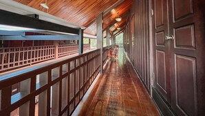 A covered corridor with wooden flooring and railings, leading to a door.