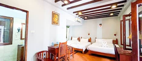 Habitación de hotel con dos camas, una mesa de madera, sillas y una estatua de Buda en la pared.