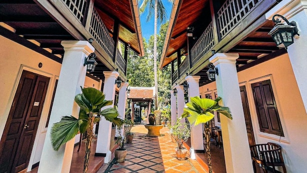 A symmetrical corridor with a central pathway, flanked by wooden balconies and white walls, leading to a palm tree and a door marked with the number 10.
