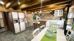 Una cocina rústica con paredes de piedra, vigas de madera y una zona de comedor con mantel verde.