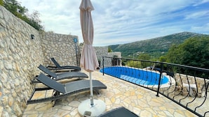 Un patio de piedra con sillones de descanso y una piscina.