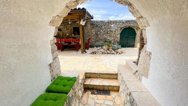 Un patio exterior con un camino de piedra, un banco de madera y un edificio rústico con puerta verde.