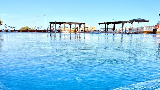 Ein Swimmingpool mit klarem, blauem Wasser, umgeben von Liegestühlen und Sonnenschirmen.