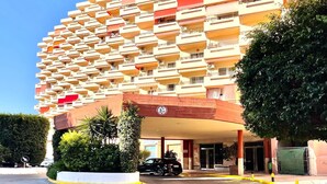 Ein mehrstöckiges Hotel mit markanter Fassade, einem Parkplatz und blauem Himmel.