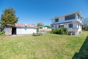Une maison à deux étages avec un toit végétalisé, un petit abri de jardin et une table de pique-nique dans une cour verdoyante.