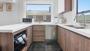 Ett modernt kök med inbyggd ugn, mikrovågsugn och diskmaskin. Köket har träskåp, ett stort fönster och utsikt över en närliggande byggnad.