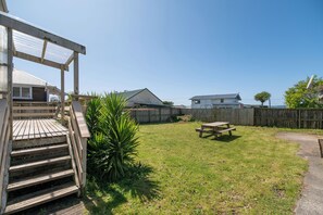 Un jardin avec une terrasse en bois, une table de pique-nique et une clôture en bois.