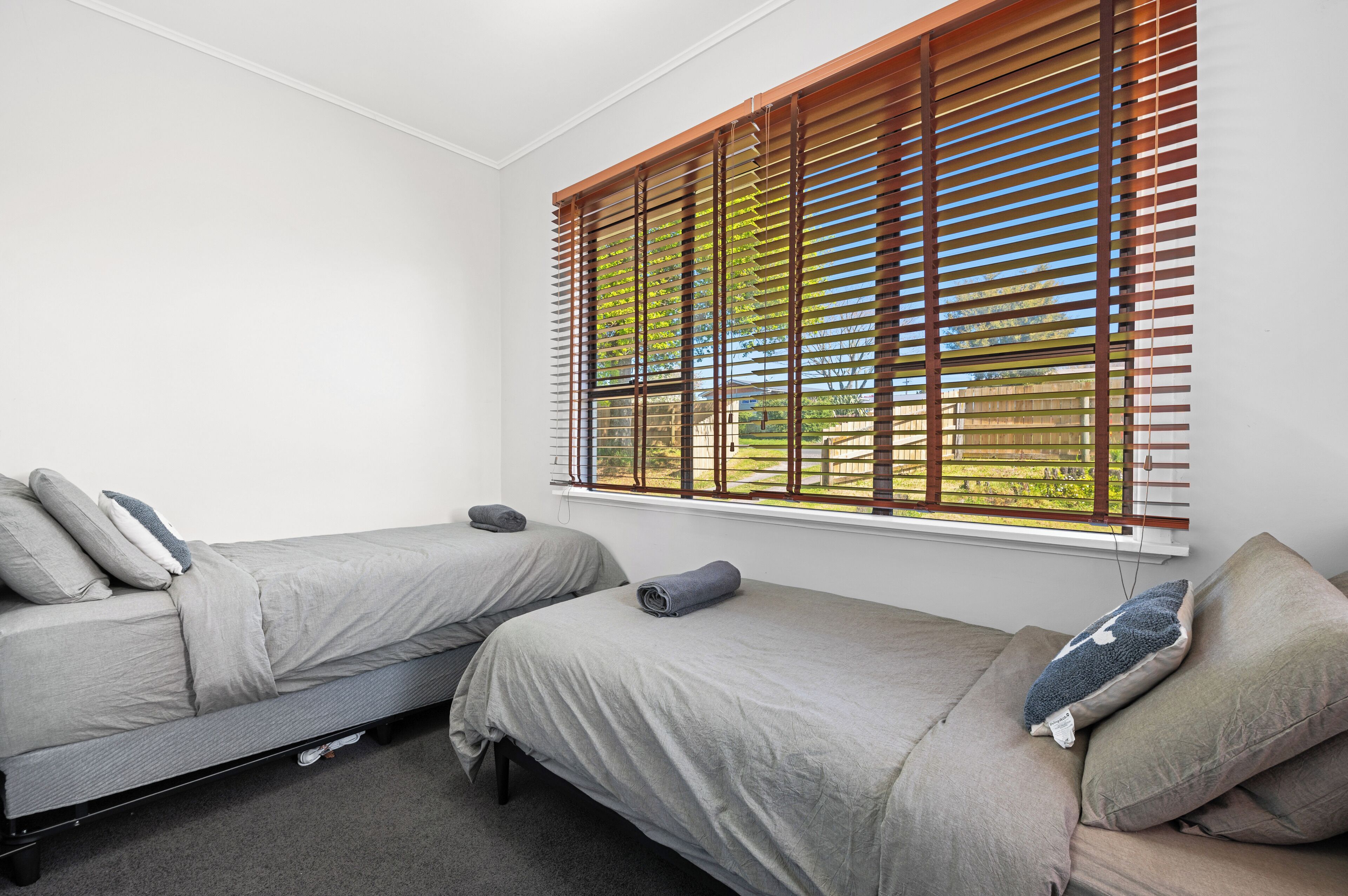 A room with two single beds, a window with blinds, and a carpeted floor.