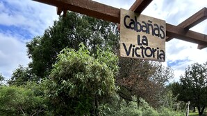 Un área de estar al aire libre con estilo rústico, con un letrero que dice 'Cabanas la Victoria', rodeada de grava y follaje.