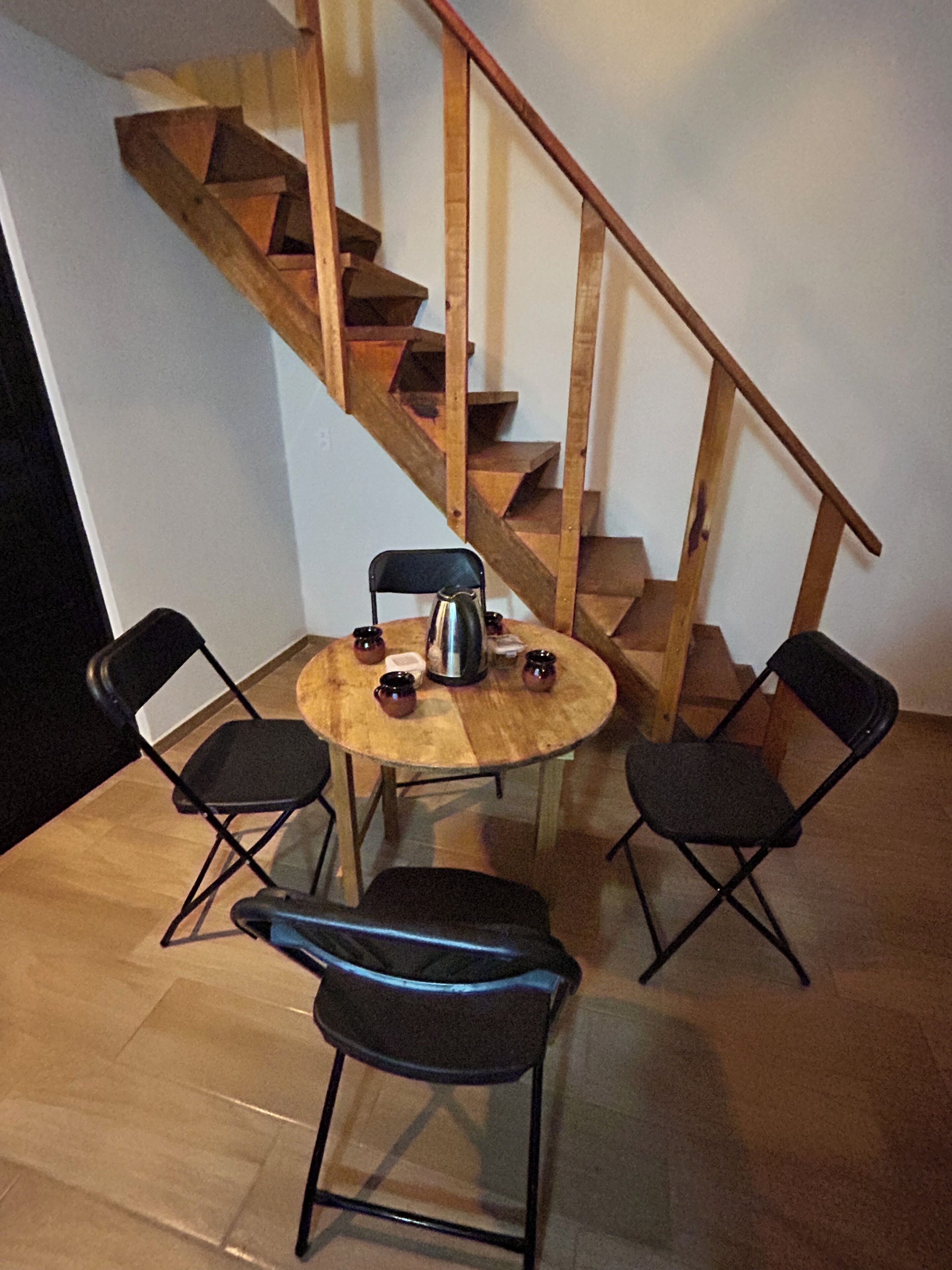 En trätrappa med ett räcke, ett runt träbord med fyra stolar och en vattenkokare på bordet.