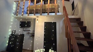 Un interior acogedor con una escalera de madera, un comedor con mesa y sillas, y un balcón con guirnaldas luminosas.