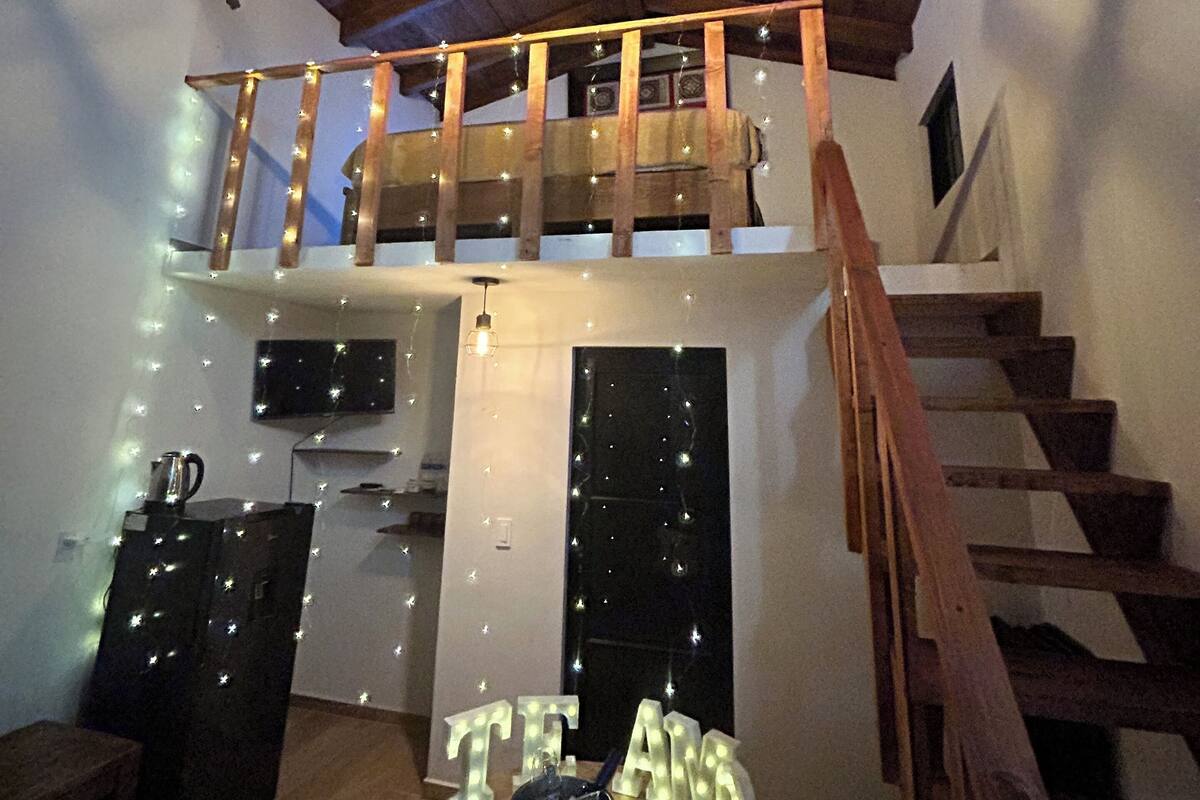 Un intérieur chaleureux avec un escalier en bois, un coin repas avec une table et des chaises, et un balcon agrémenté de guirlandes lumineuses.