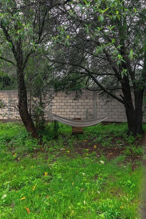 A hammock between trees in a grassy area with a brick wall in the background. - Cabañas La Victoria By GEstores (Huasca de Ocampo)