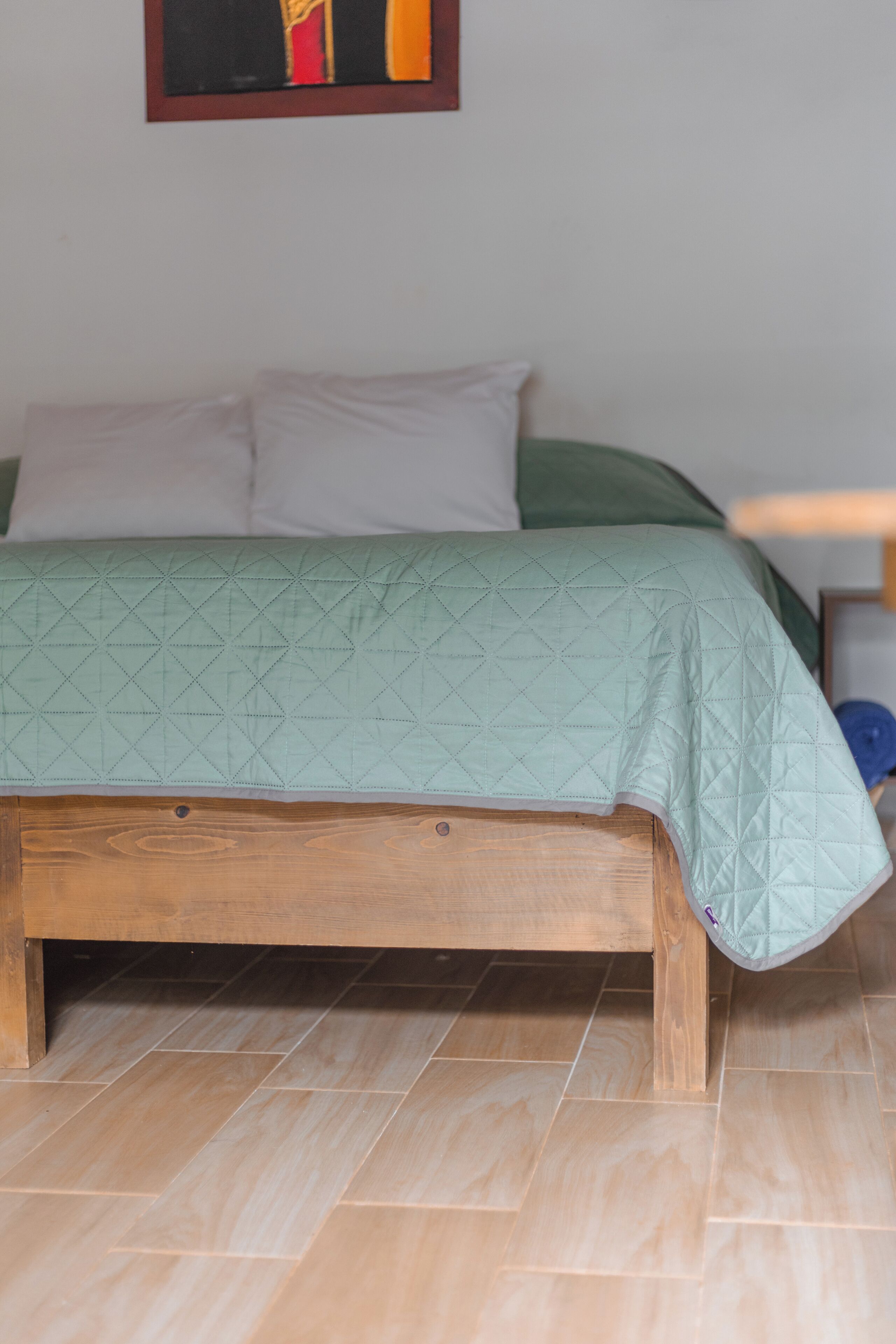 A bed with a wooden frame, a green quilt, and white pillows.