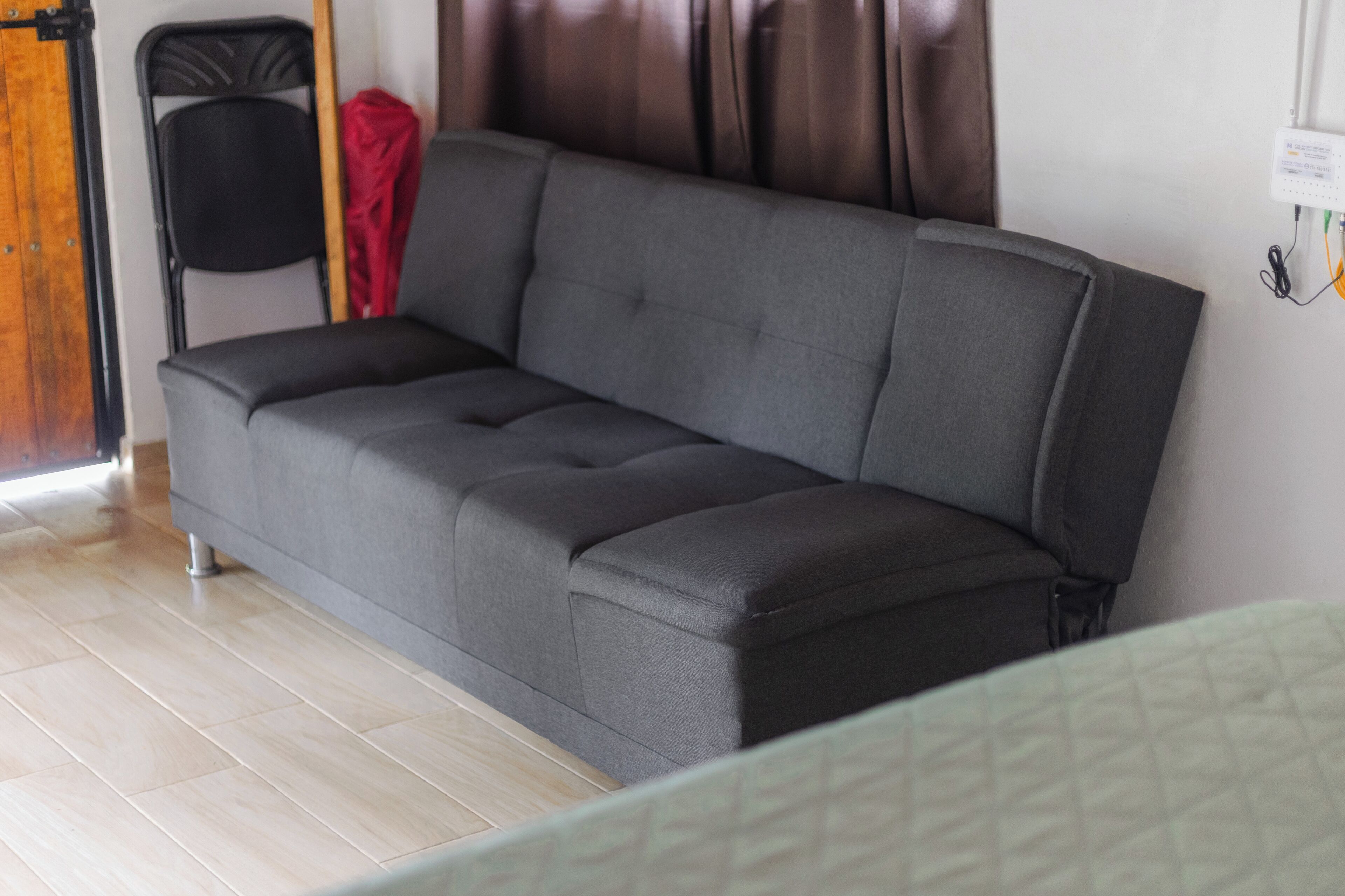 A gray sofa in a room with a wooden floor and a red jacket hanging on a chair.