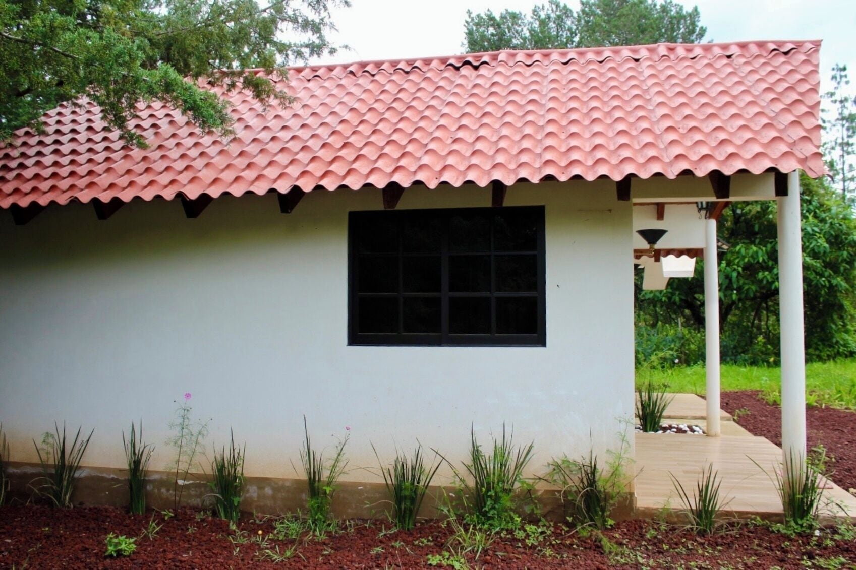 A small building with a red-tiled roof, a window, and a porch area.