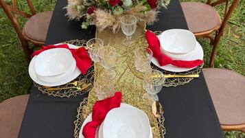 Mesa al aire libre con mantel negro, detalles dorados, servilletas rojas y un centro de mesa floral.