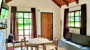 Una habitación con techo de madera alto, una mesa redonda con sillas, un sofá y un televisor sobre un mueble.