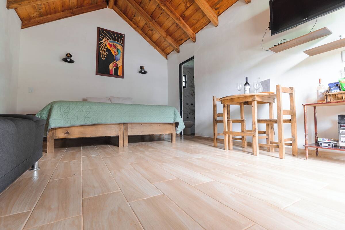 Une pièce comprenant un lit, une table avec des chaises, un téléviseur et un tableau accroché au mur.