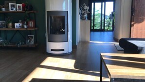 A modern living room with a wood-burning stove, a wooden coffee table, and a bookshelf with personal items.