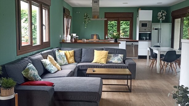 A modern kitchen with a dining area, a grey sectional sofa, and a wooden coffee table.